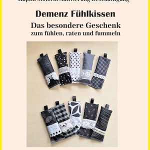May include: A selection of sensory pillows in black and white designs, such as polka dots and floral patterns, with lace detailing. Each pillow has a small black loop. The image includes the text "Demenz Fühlkissen" and "Beispielbild".