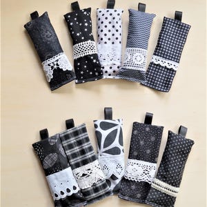 Puede incluir: Ocho objetos de tela en blanco y negro con lazos, con diversos patrones como estrellas, lunares y diseños florales. Algunos tienen adornos de encaje blanco. Los artículos están dispuestos sobre una superficie clara, mostrando una variedad de diseños textiles.