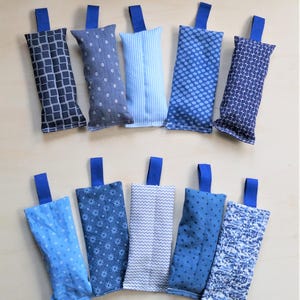 Puede incluir: Diez saquitos rectangulares de tela azul, con diversos estampados como rayas y lunares. Cada saquito tiene una presilla de tela azul. Dispuestos sobre una superficie de madera clara.