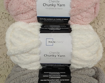 May include: Three skeins of Mainstays Chenille Chunky Yarn in pink, white, and gray. The yarn is packaged with a label that includes instructions for making a round pillow, a cylinder pillow, and an arm knit throw. The label also includes the text "Hilo grueso de felpilla" which is Spanish for "thick chenille yarn".