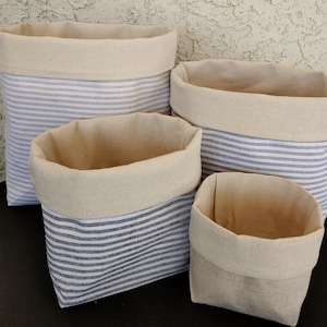May include: Four striped fabric storage baskets in various sizes. The baskets are made of a natural canvas fabric with a white and gray striped pattern. The baskets are ideal for organizing and storing items in a home or office.