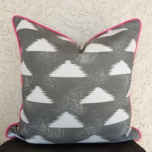 May include: A gray and white geometric patterned throw pillow with a hot pink trim.