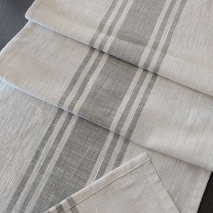 May include: A white table runner with gray stripes. The runner is folded in thirds, showing the pattern and texture of the fabric.