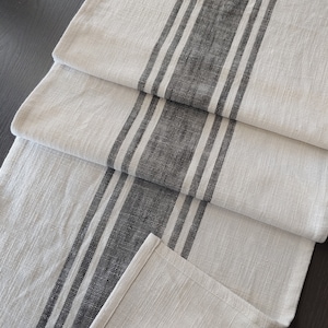 May include: A white linen table runner with three black stripes running down the length of the runner.