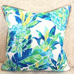 May include: A white pillow with a blue, green, and yellow pineapple leaf pattern. The pillow has a brown burlap trim.