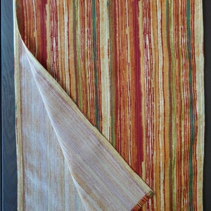May include: A striped table runner with a beige and brown color scheme. The runner is folded in half, revealing a beige underside.