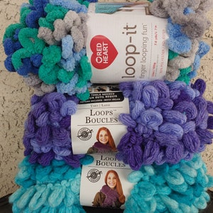 May include: Three skeins of yarn in shades of teal, purple, and gray. The yarn is a bulky, looped texture. The yarn is labeled "Loop-it" and "Loops Boucles".
