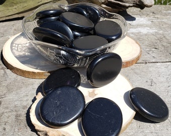 May include: A bowl filled with smooth, black obsidian stones. The stones are arranged in a circular pattern and are surrounded by a white background.