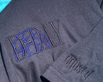 May include: Black t-shirt with a blue and black embroidered design that says "DAY" and "august" on the sleeve.