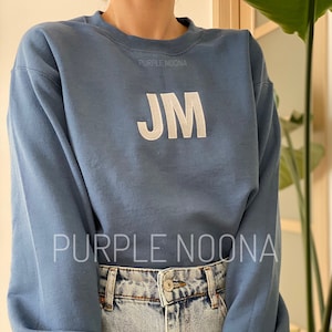 May include: A blue sweatshirt with white embroidered letters "JM" and the text "PURPLE NOONA" on the front. The sweatshirt is size S.