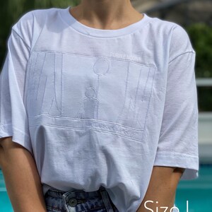 May include: White t-shirt with a graphic of a person holding a balloon and the text "PURPLE NOONA" and "Seasonalcity". The t-shirt is size L.