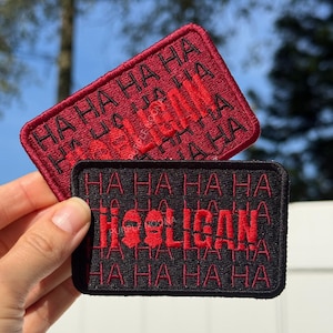 Può includere: Due toppe rettangolari con testo ricamato. Una è nera con testo rosso "HA HA HA HA Hooligan HA HA HA HA". L'altra è rossa con testo nero "HA HA HA HA Hooligan HA HA HA HA".