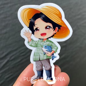 May include: A sticker featuring a cartoon illustration of a person wearing a straw hat, green plaid shirt, gray pants, and black boots. The person is holding a blue fish and waving. The text "PURPLE NOONA" is visible.