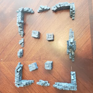 May include: A set of 12 grey miniature stone wall pieces for model building or tabletop gaming. The pieces are made of a textured plastic and are designed to look like weathered stone.