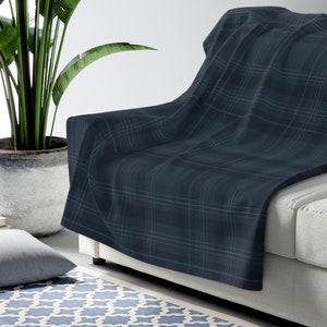 May include: A dark blue plaid throw blanket draped over a white sofa. The blanket has a subtle sheen and is made of a soft, plush material.