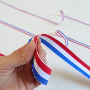 Peut inclure: Gros plan sur une main tenant un ruban rouge, blanc et bleu. Le ruban est rayé et a une texture lisse.