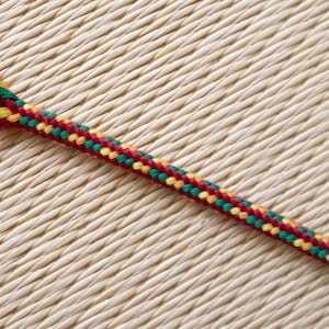 May include: A close-up of a red, yellow and green braided cord. The cord is lying on a woven surface.