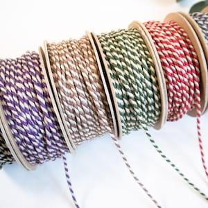 May include: Six spools of baker's twine in various colors, including black, purple, brown, green, red, and blue. Each spool has a white stripe running along the twine.