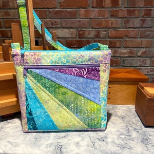 May include: A blue, green, and purple patchwork fabric crossbody bag with a zipper closure. The bag has a light yellow background with white polka dots.