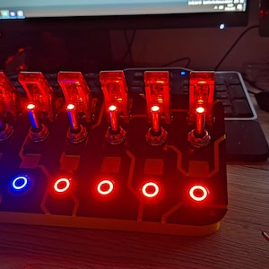 May include: A red and black electronic device with six toggle switches and six LED lights. The lights are red and blue. The device is on a wooden surface.