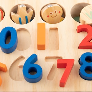 K&ouml;nnte beinhalten: Holz-Lernspielzeug mit bunten Zahlen und Formen. Die Zahlen sind blau, orange und rot. Die Formen umfassen einen Fisch, eine Blume und einen Lebkuchenmann. Entwickelt f&uuml;r fr&uuml;hes Lernen und Zahlenverst&auml;ndnis.
