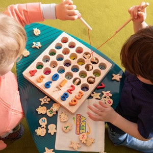 K&ouml;nnte beinhalten: Holz-Lernspielzeug mit bunten Zahlen und Buchstaben. Kinder spielen mit einem Holz-Angelspiel, bei dem sie mit einer Magnetangel Holzformen fischen. Das Spiel enth&auml;lt ein Holzbrett mit L&ouml;chern und einen Stoffbeutel mit dem Text "AXEL ADVENTURES".