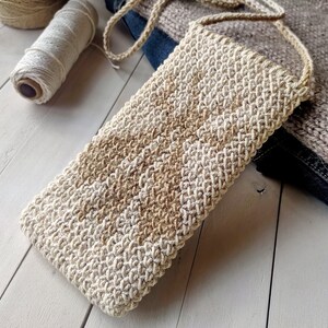May include: A beige and brown crocheted phone pouch with a long strap. The pouch is made with a textured stitch and has a simple, minimalist design.