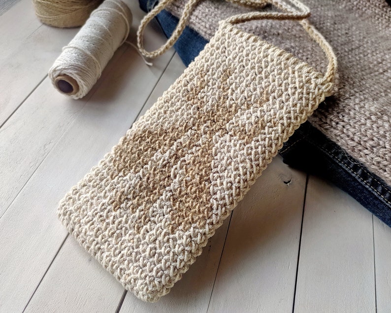 May include: A beige and brown crocheted phone pouch with a long strap. The pouch is made with a textured stitch and has a simple, minimalist design.