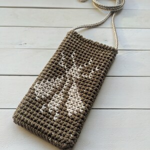 May include: A brown crocheted bag with a white crocheted design of two deer. The bag has a long strap for carrying over the shoulder.