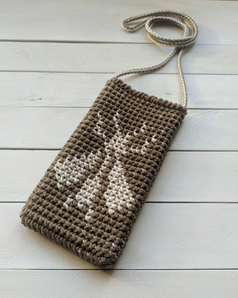 May include: A brown crocheted bag with a white crocheted design of two deer. The bag has a long strap for carrying over the shoulder.