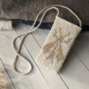 May include: A small crocheted bag with a beige and brown geometric pattern. The bag has a long strap and is made of natural fibers.
