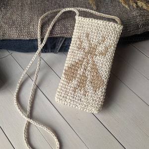 May include: A beige crocheted crossbody bag with a brown geometric pattern. The bag has a long strap and is made of a natural fiber.
