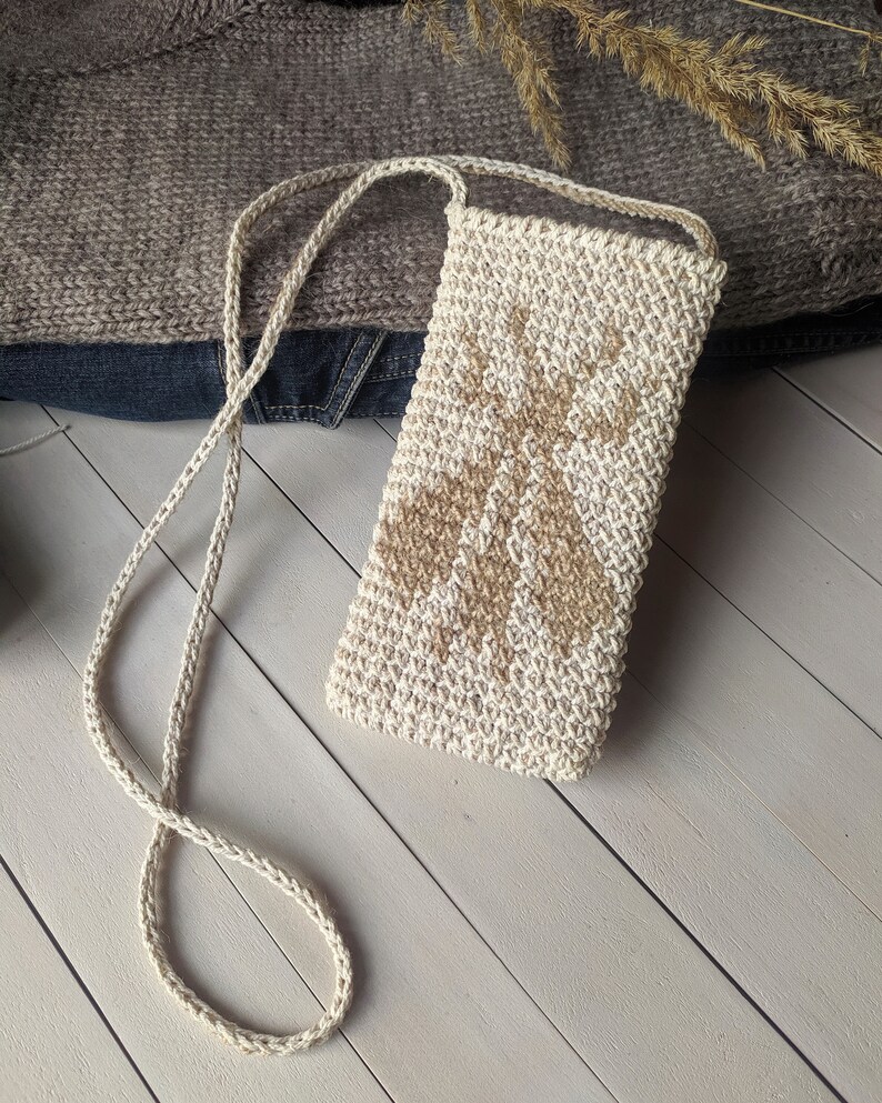 May include: A beige crocheted crossbody bag with a brown geometric pattern. The bag has a long strap and is made of a natural fiber.
