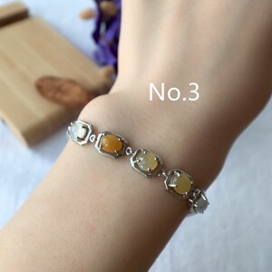 May include: A silver bracelet with a row of oval-shaped gemstones in shades of yellow and orange. The bracelet is on a person's wrist and the text "No. 3" is visible above the bracelet.