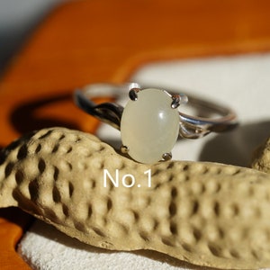 May include: A silver ring with a white oval gemstone. The ring is set on a textured surface with the text "No. 1" visible.
