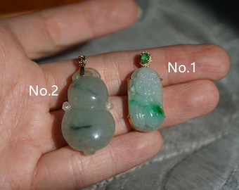 May include: Two jade pendants on a hand. The pendant on the left is a green jade gourd with gold accents. The pendant on the right is a green jade figure of a person with gold accents. The pendants are labeled No. 2 and No. 1 respectively.