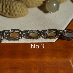 May include: A silver bracelet with five oval-shaped stones set in square frames. The stones are a mix of white, yellow, and light brown. The bracelet is labeled "No. 3".