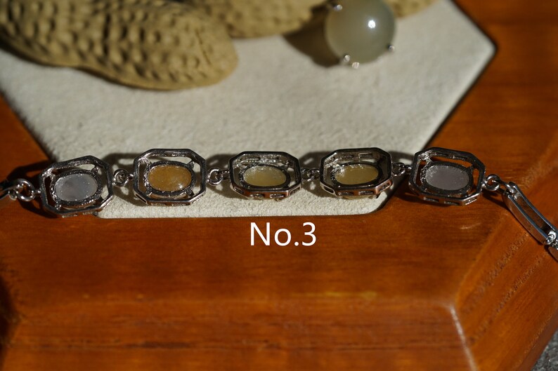 May include: A silver bracelet with five oval-shaped stones set in square frames. The stones are a mix of white, yellow, and light brown. The bracelet is labeled "No. 3".