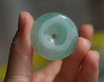 Può includere: Un ciondolo in giada verde chiaro a forma di ciambella con un foro al centro. Il ciondolo è liscio e lucido.