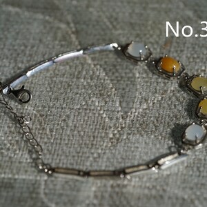 May include: A silver bracelet with a chain and a clasp. The bracelet has five stones, two white, one yellow, and two light yellow.