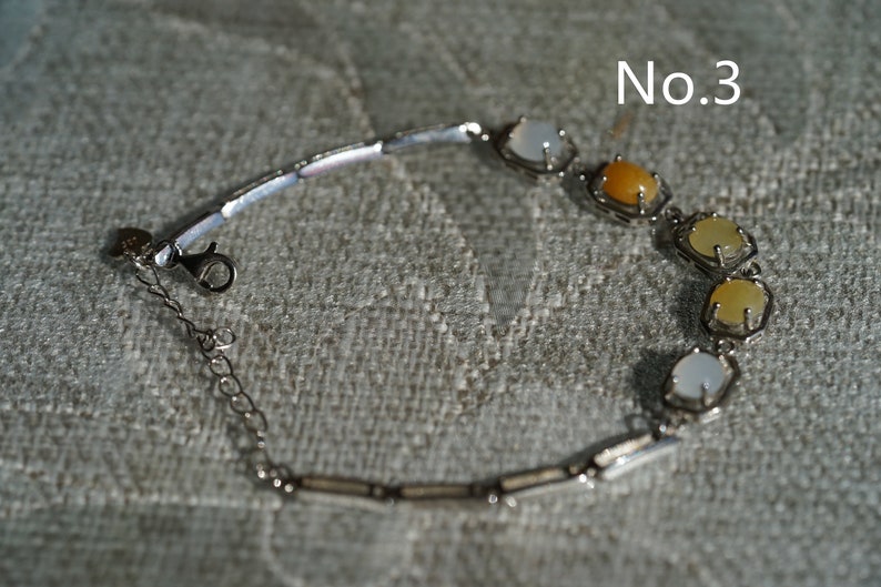 May include: A silver bracelet with a chain and a clasp. The bracelet has five stones, two white, one yellow, and two light yellow.