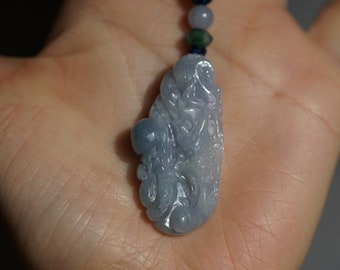 May include: A light blue jade pendant carved with a detailed design of a mythical creature. The pendant is hanging from a beaded necklace.