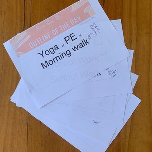 May include: A stack of white paper sheets with the text "OUTLINE OF THE DAY" in peach and the options "Yoga or PE or Morning walk". The papers are on a wooden surface.