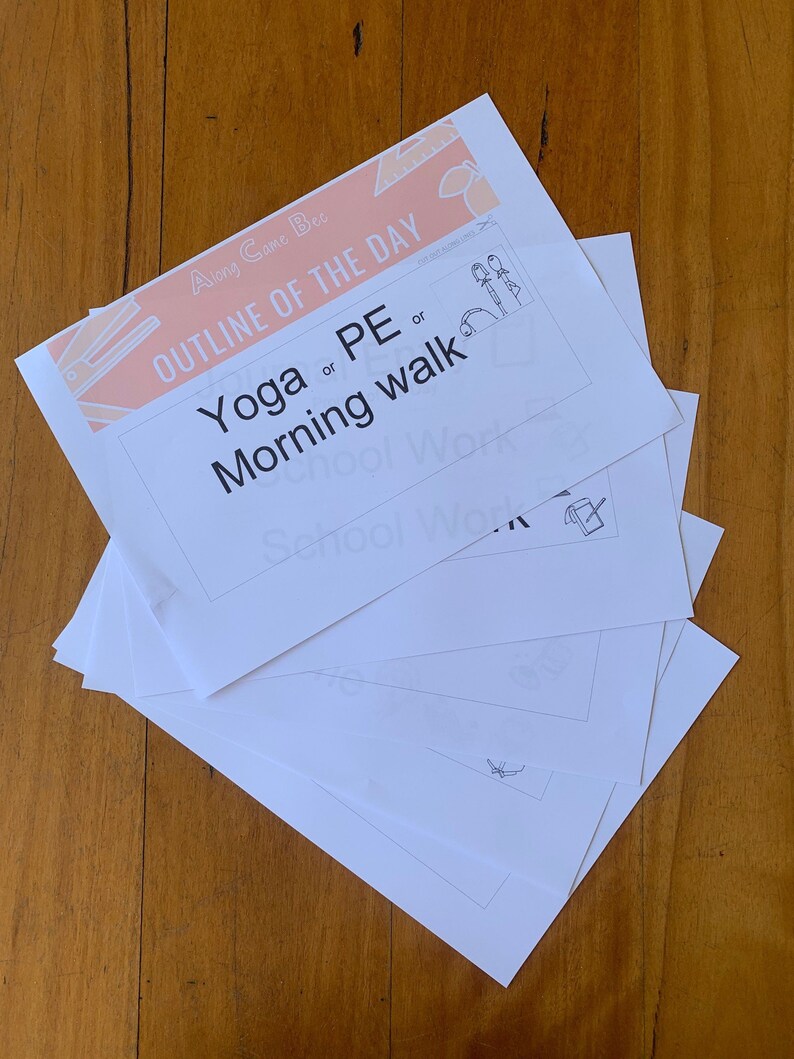 May include: A stack of white paper sheets with the text "OUTLINE OF THE DAY" in peach and the options "Yoga or PE or Morning walk". The papers are on a wooden surface.