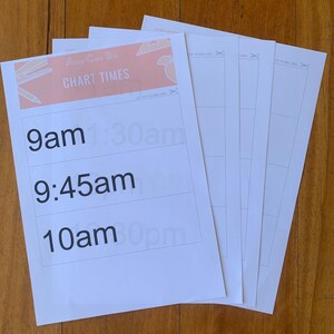 May include: A stack of white paper sheets with the text "Along Came Bee CHART TIMES" in peach and black. The sheets have time slots printed on them, including 9am, 9:45am, and 10am. The sheets are on a wooden surface.