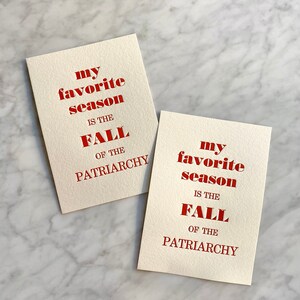 May include: Two cards with the text "my favourite season is the fall of the patriarchy" printed in red on a white background.