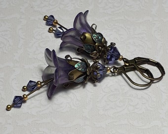May include: Purple flower dangle earrings with gold accents and crystal beads. The earrings have a bell-shaped flower design with a bronze hook.