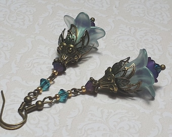 Puede incluir: Un par de pendientes colgantes con un dije de flor azul claro, una cuenta morada y una cadena de bronce con cuentas turquesa.