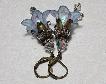 May include: A pair of iridescent blue flower earrings with crystal accents and bronze-colored metal accents. The earrings have a hook closure.