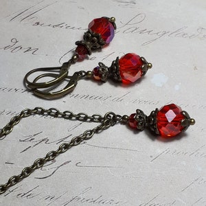 May include: A set of red glass earrings and a necklace with antique bronze chain and accents. The earrings have a teardrop shape and the necklace has a pendant with a teardrop shape.